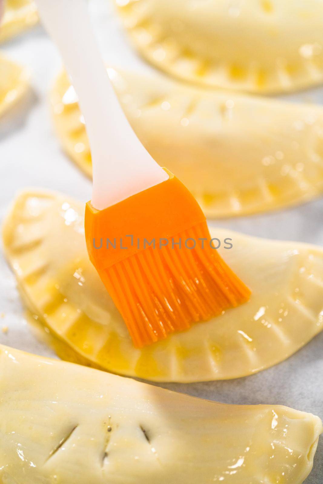 Brushing uncooked empanadas with blueberries with egg wash.