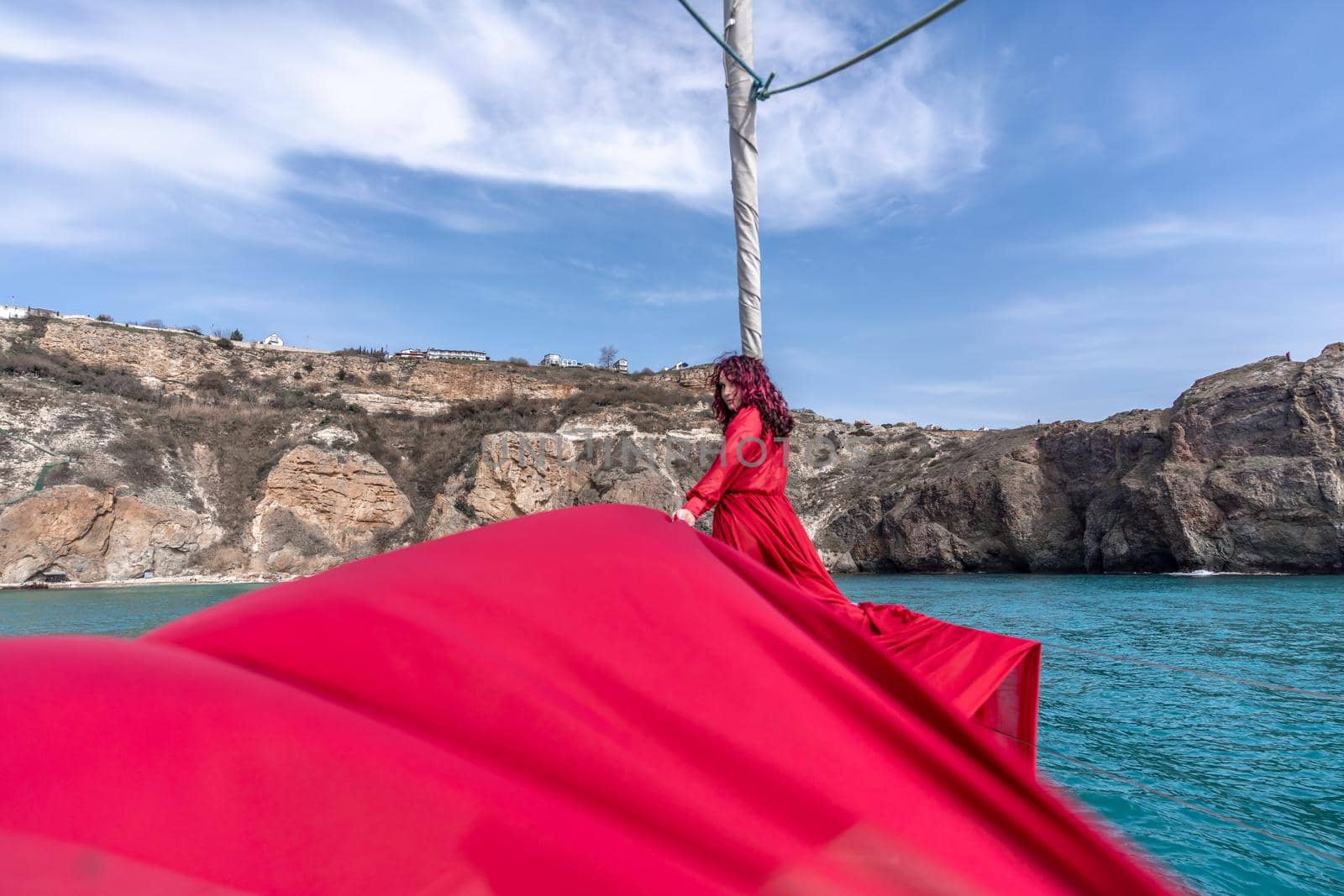 Attractive middle-aged woman in a red dress on a yacht on a summer day. Luxury summer adventure, outdoor activities