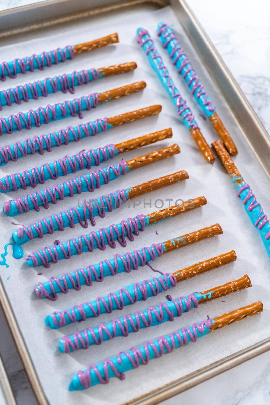 Drizzled with chocolate pretzel rods drying on a baking sheet lined with parchment paper.