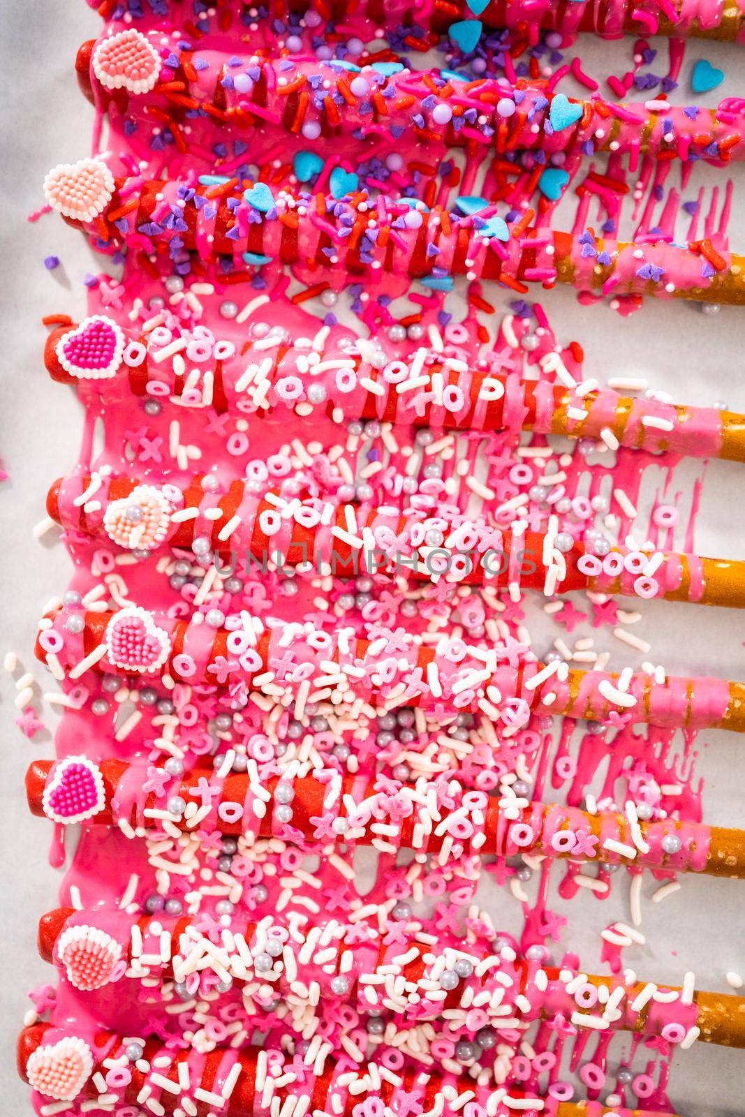 Drizzling melted chocolate over chocolate-dipped pretzels rods and decorating with sprinkles to make chocolate-covered pretzel rods for Valentine's Day.