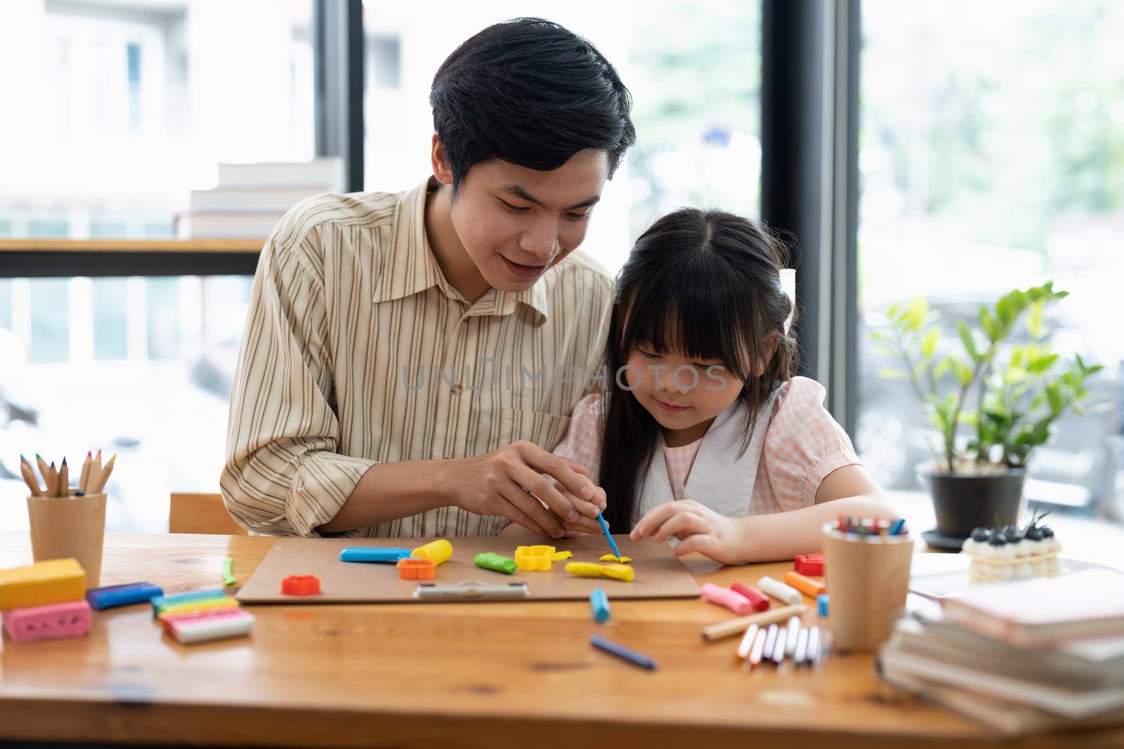 Young asian father and daughter plasticine or play dough on a table dough together by nateemee