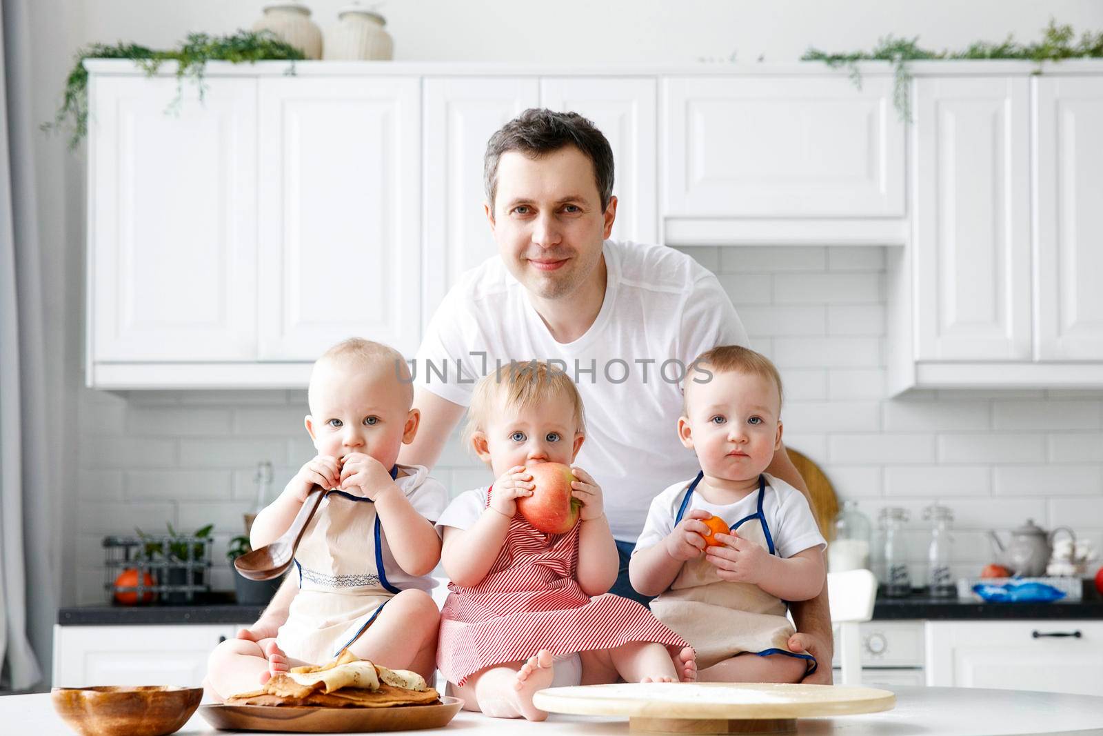 triplets, two boys and a girl in the arms of a happy father. kitchen background by Ramanouskaya