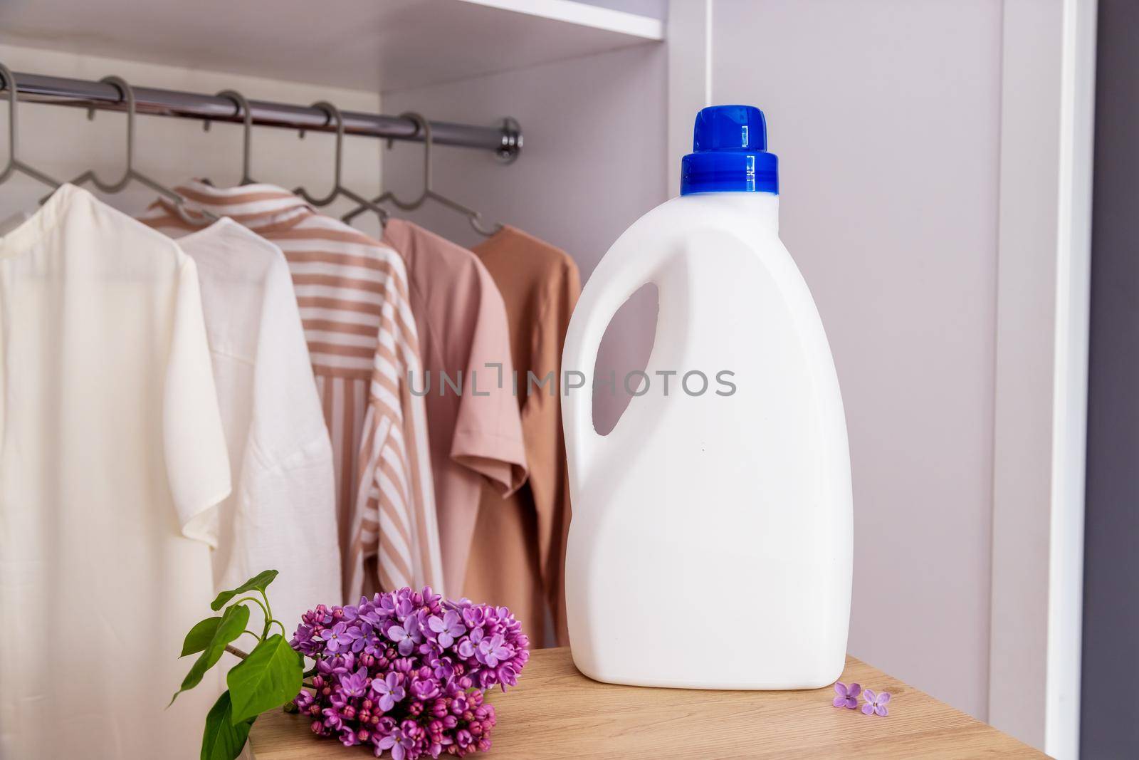 Eco Design Mockup of Empty Bottles Packing Laundry Detergent against Closet Background with Clothes in Neutral Colors. Place for text. Bio organic product. Lilac branch, fresh scent