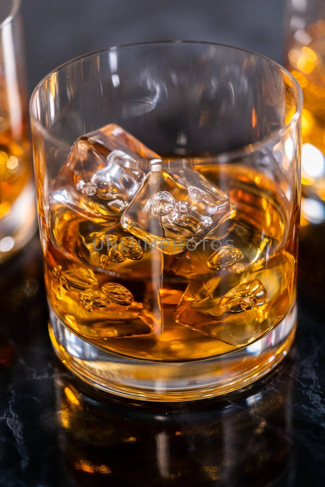 Scotch on the rocks in whiskey glass on a black marble surface.