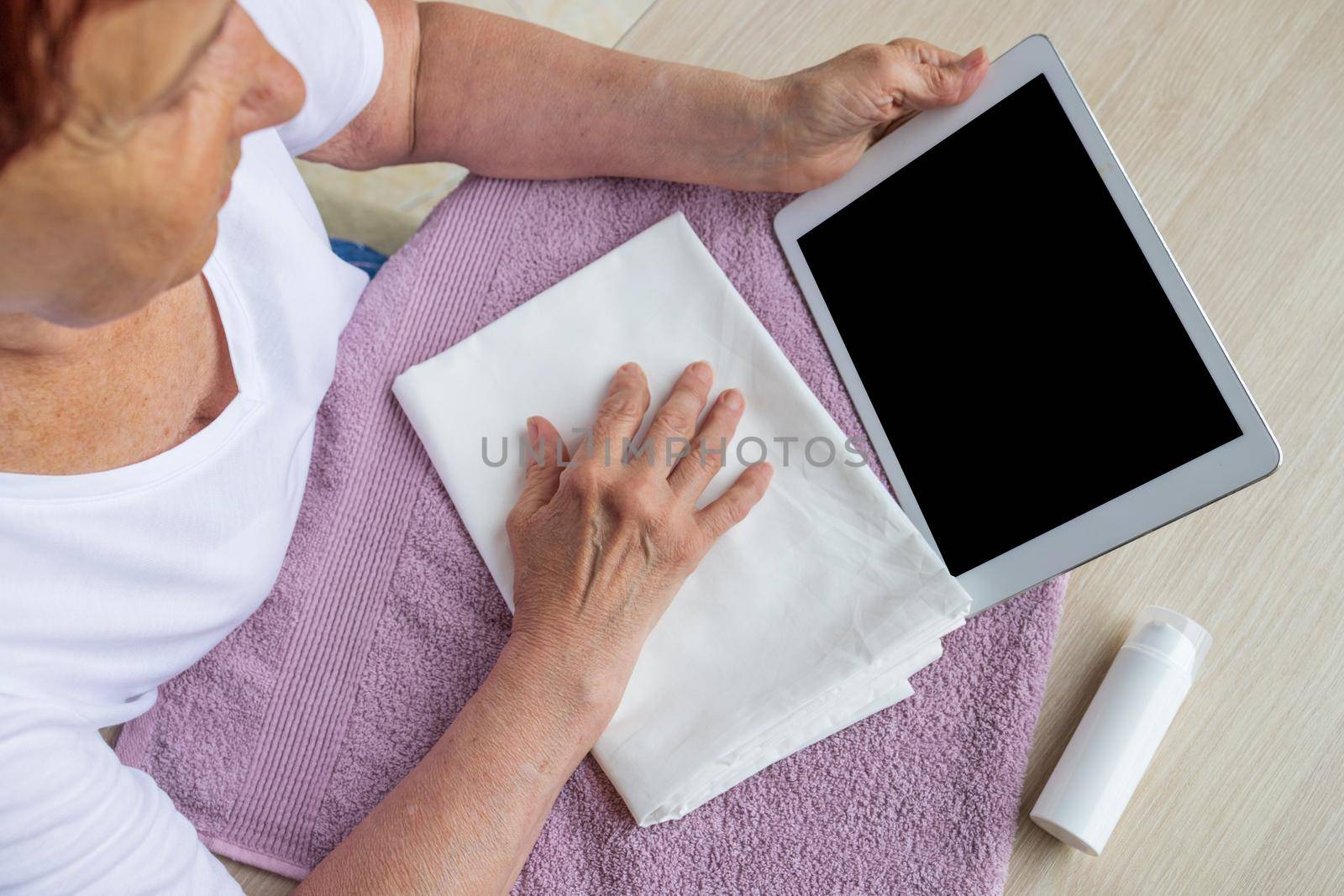 close-up, top view. An elderly woman with arthritis and joint disease holds a tablet in her hands. Online consultation concept, template, mockup for medical app or online consultation