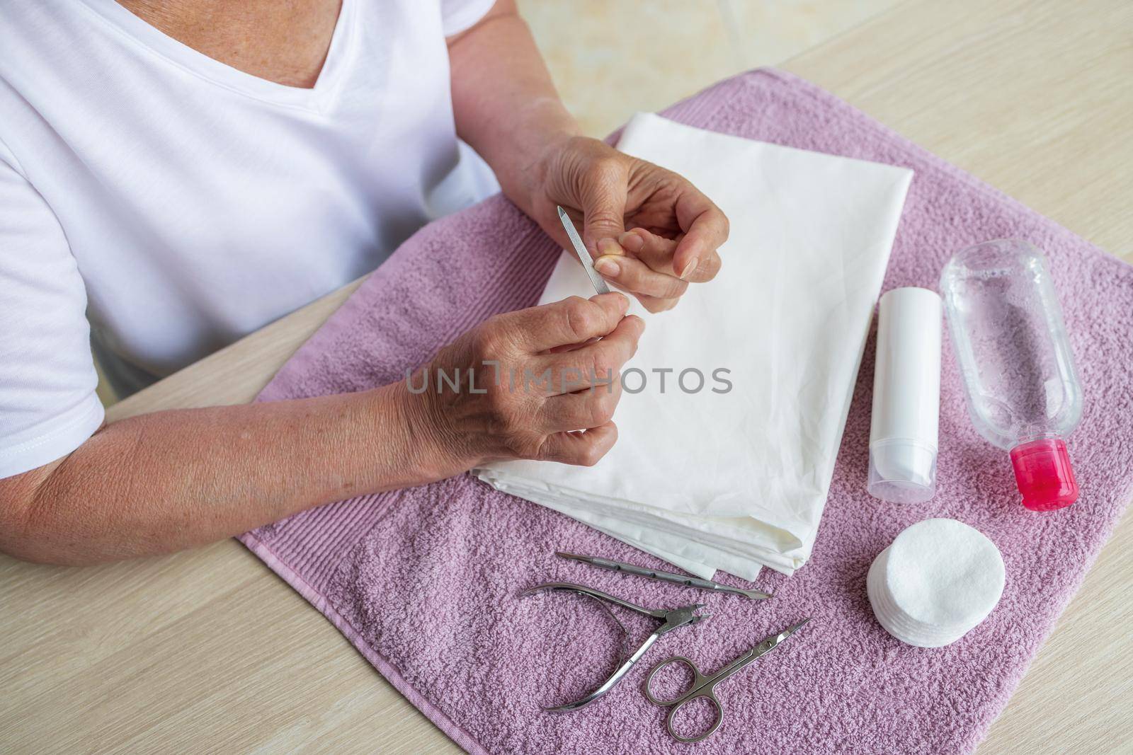 Close-up, top view, the hands of elderly woman, makes herself manicure at home. The concept of taking care of yourself, caring for the elderly in a swamp mine. Special products for hand rejuvenation