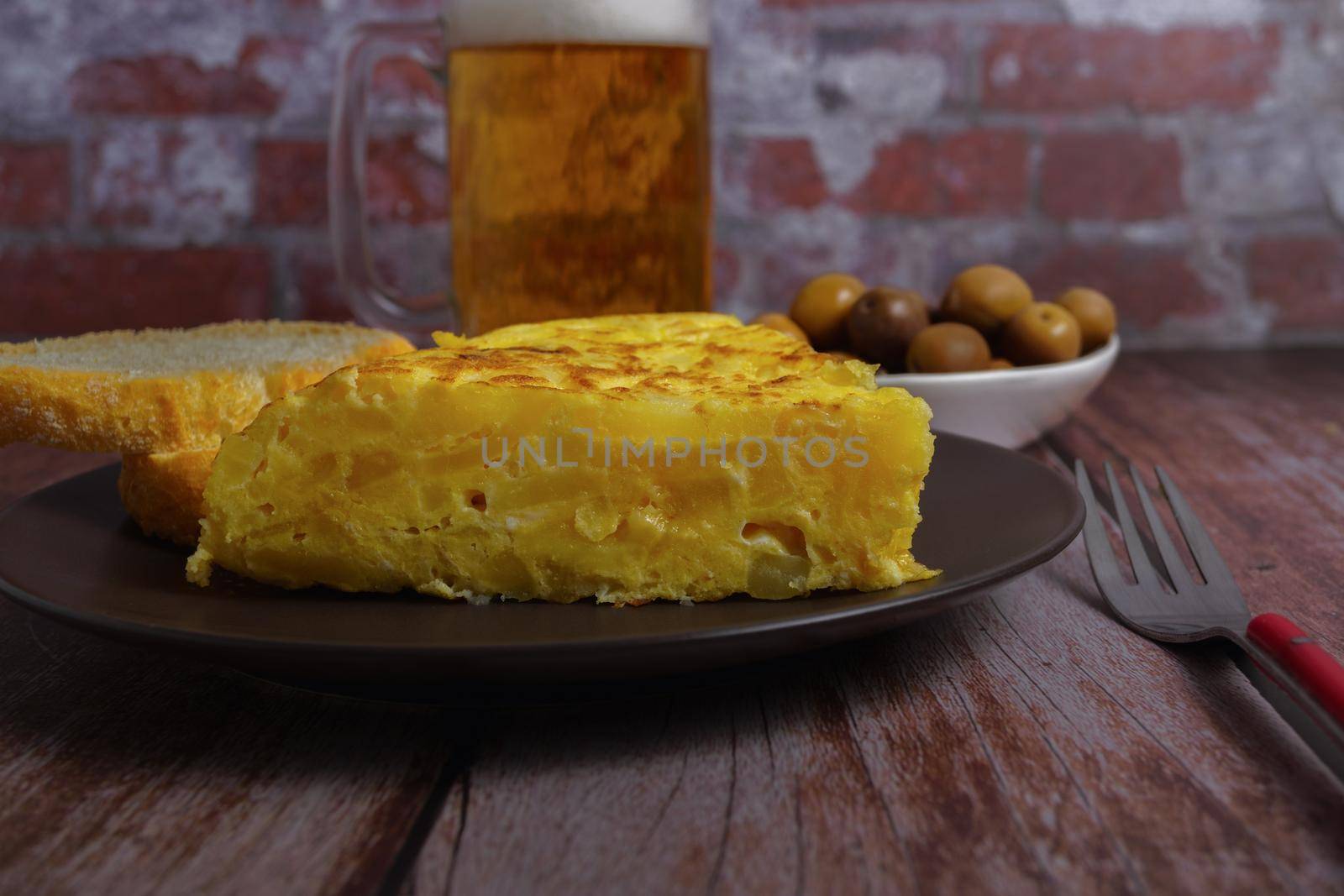 top view of typical spanish potato omelette with bread, cutlery and beer mug by joseantona