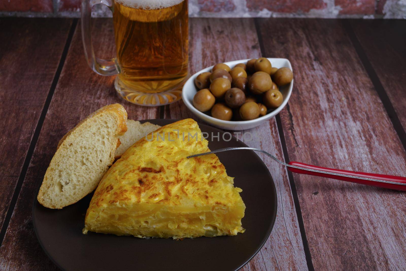top view of typical spanish potato omelette with bread, cutlery and beer mug by joseantona