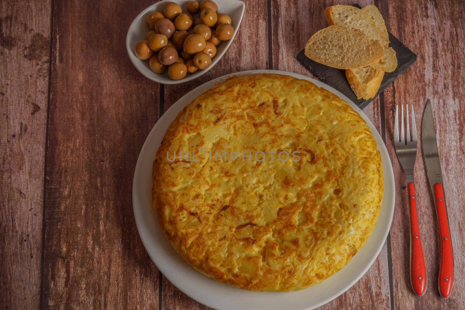 top view of typical spanish potato omelet with olives and slices of bread