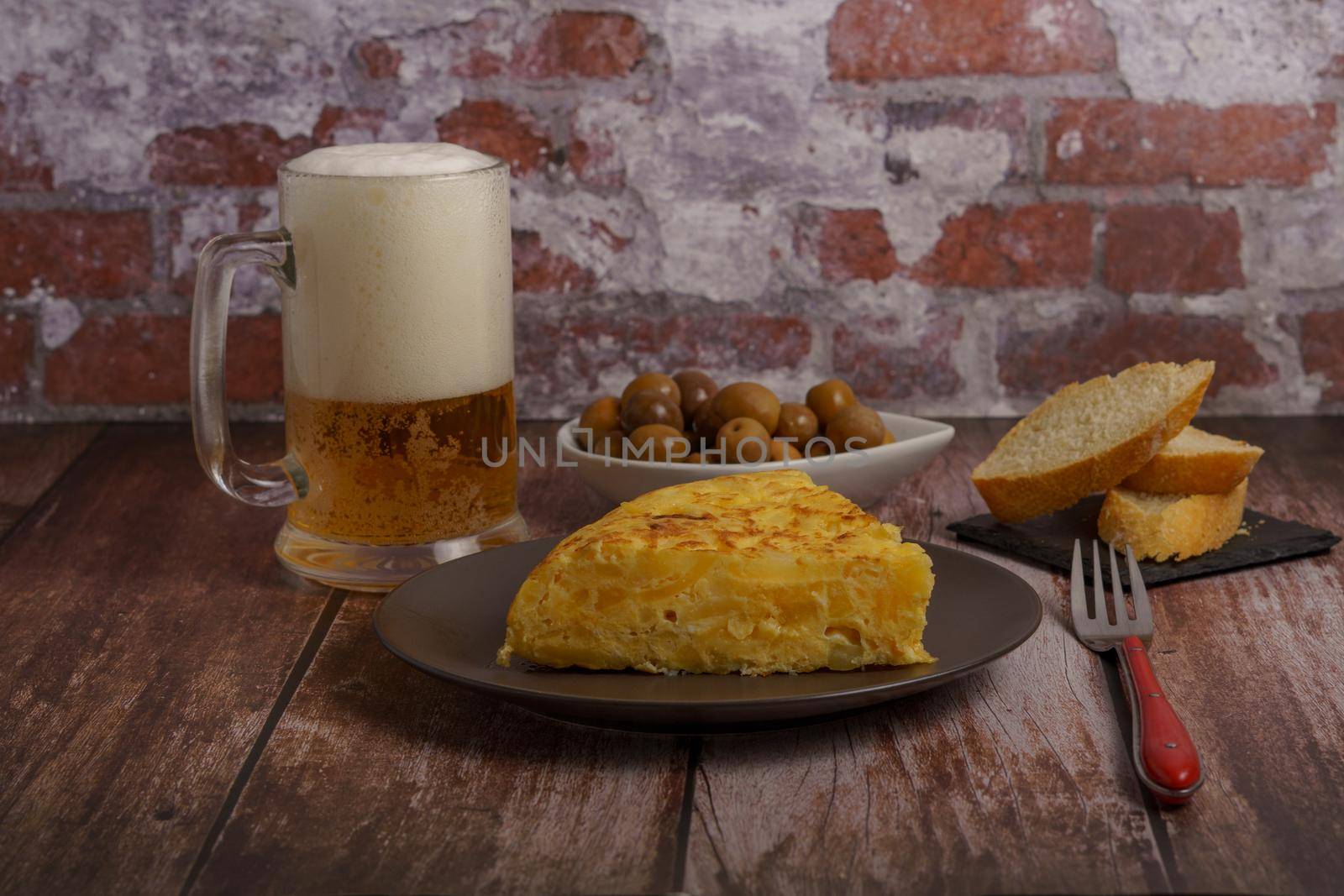 typical spanish potato omelette with bread, cutlery and beer mug by joseantona