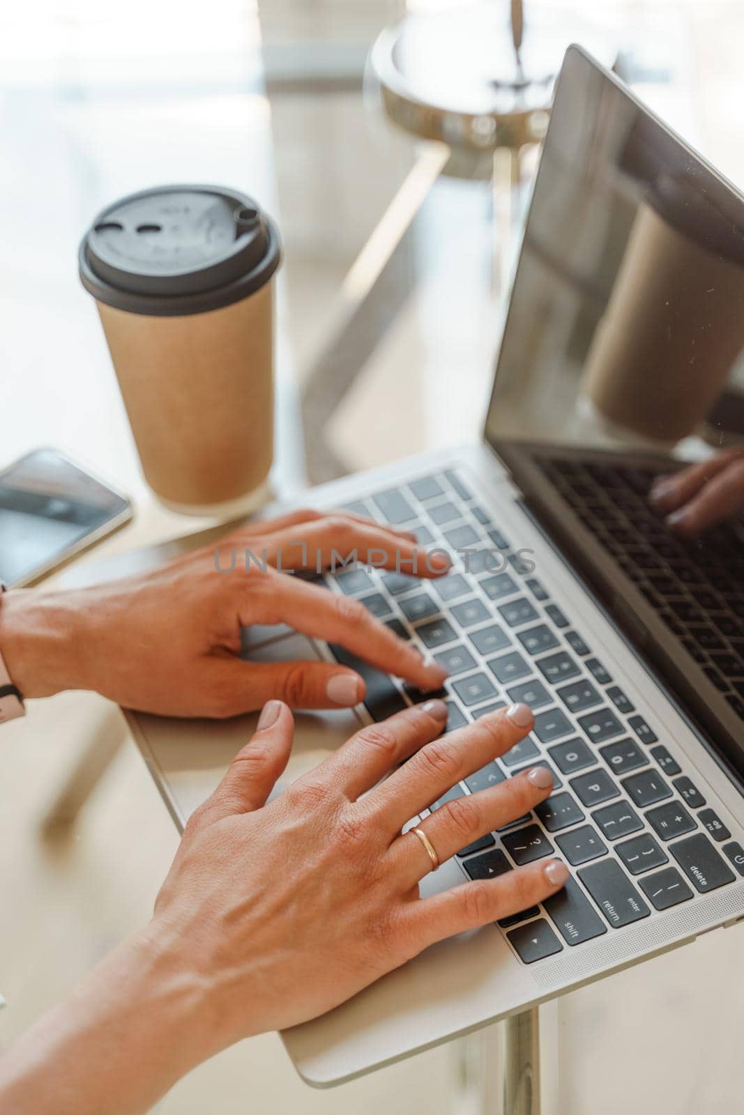 Hands typing on a computer keyboard over a white office table with a cup of coffee and supplies, top view