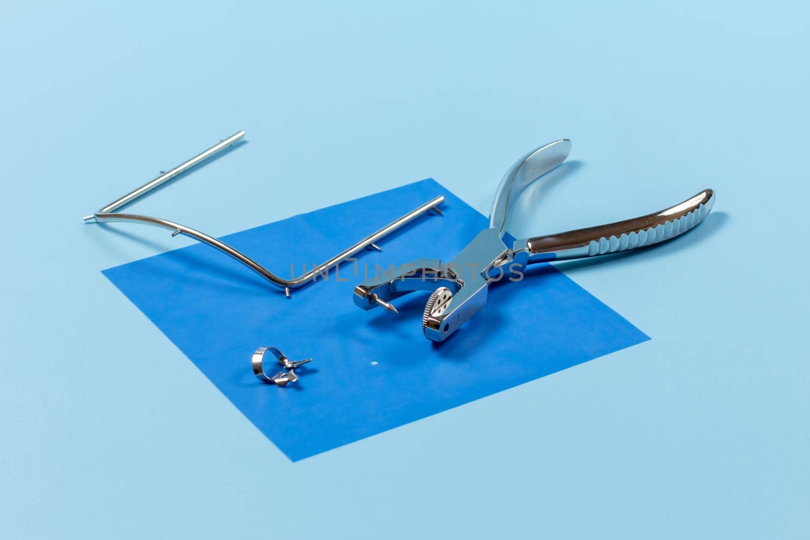 Dental hole punch, the clamp, the metal frame and the rubber dam on the blue background. Medical tools concept.