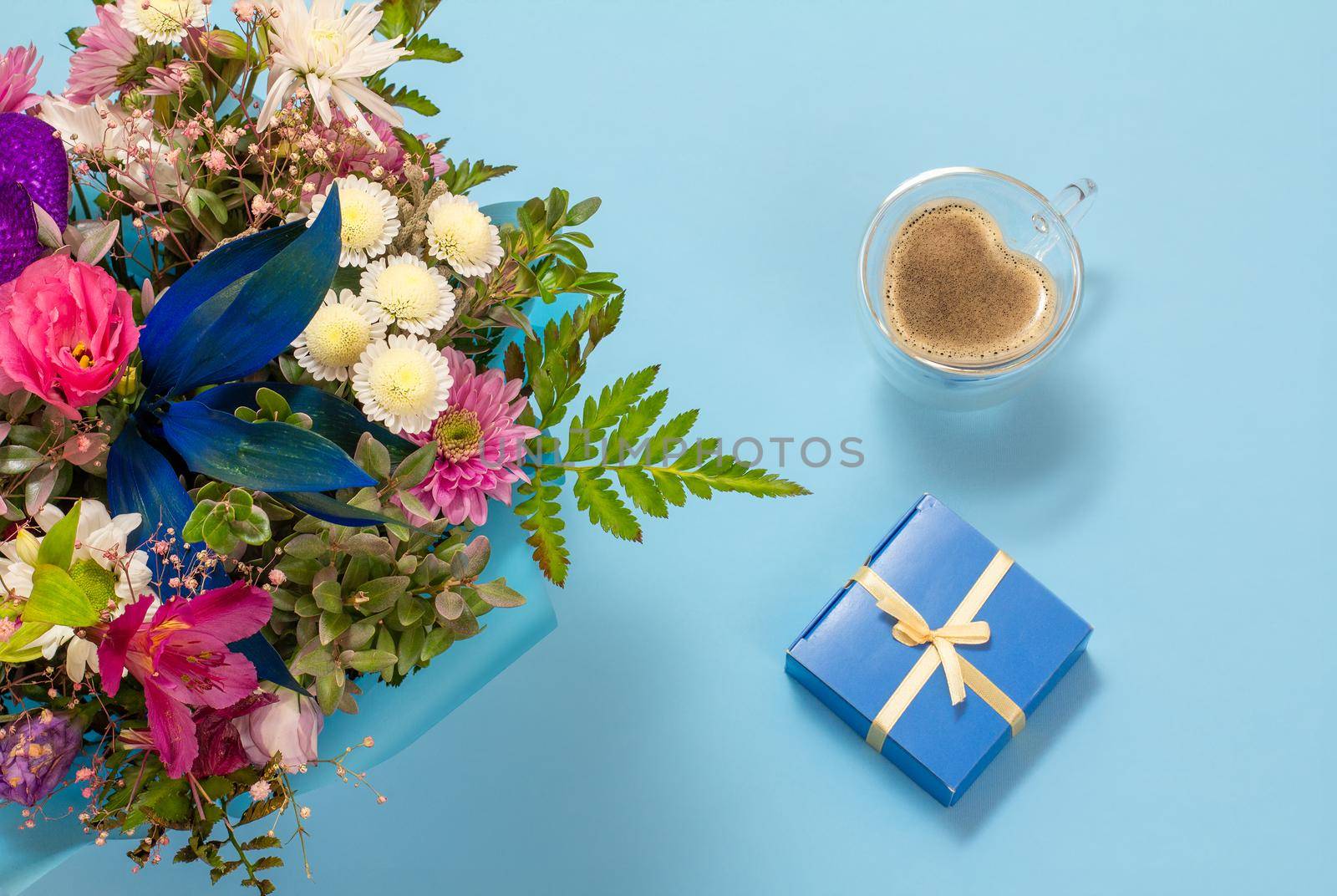 Cup of coffee, a gift box and flowers on the blue background. Top view.