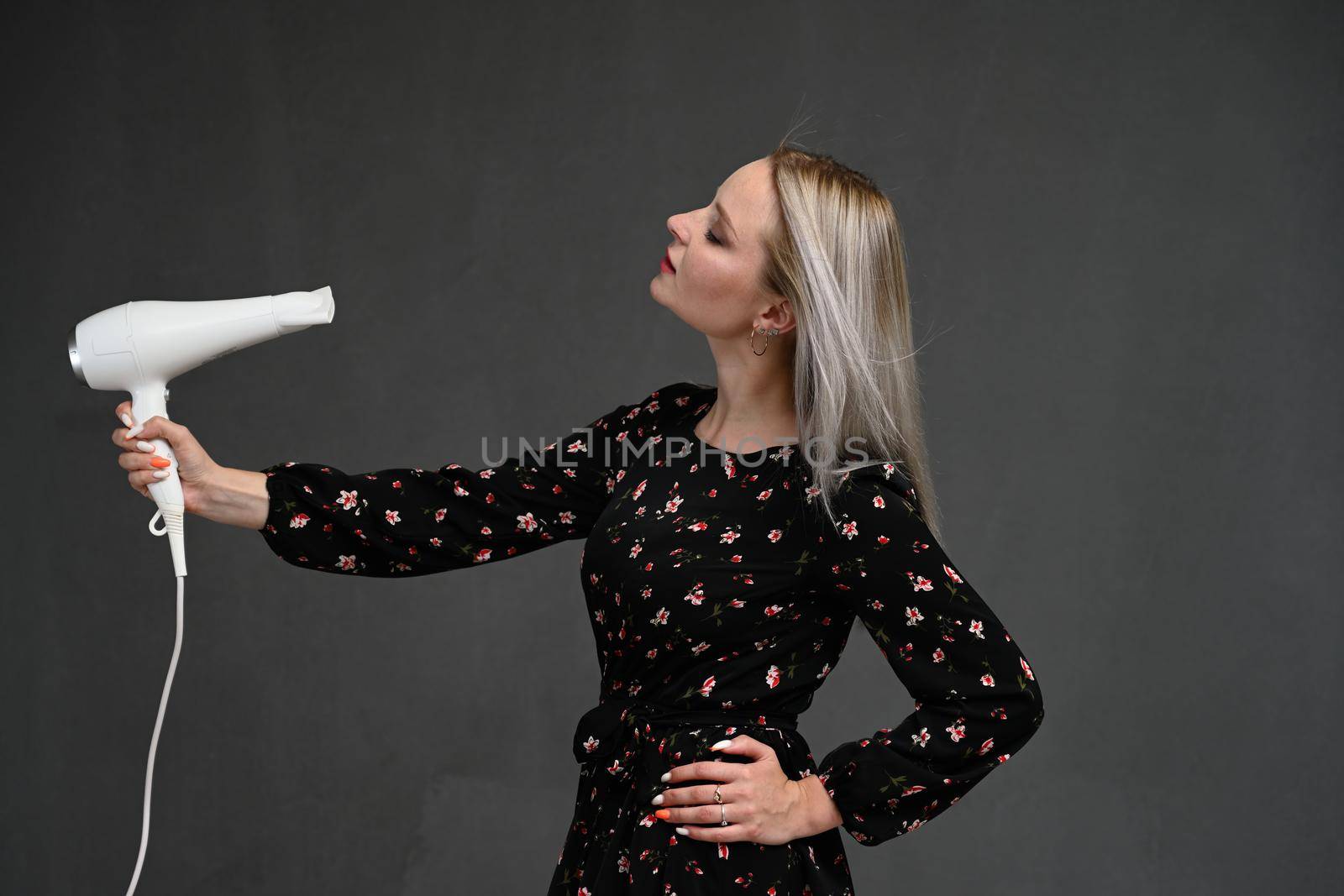 beautiful blondy girl blowing her hair with hairdryer, screaming - isolated on gray