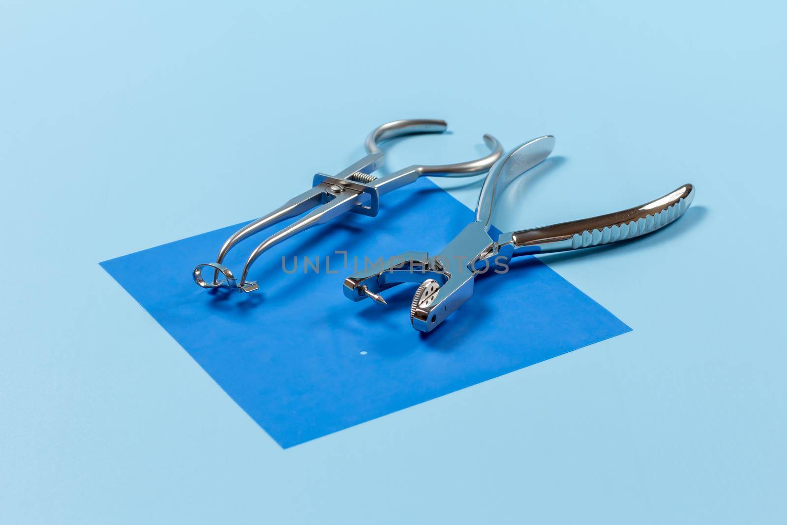 Dental hole punch and a rubber dam forceps with the clamp on the blue rubber dam. Medical tools concept.