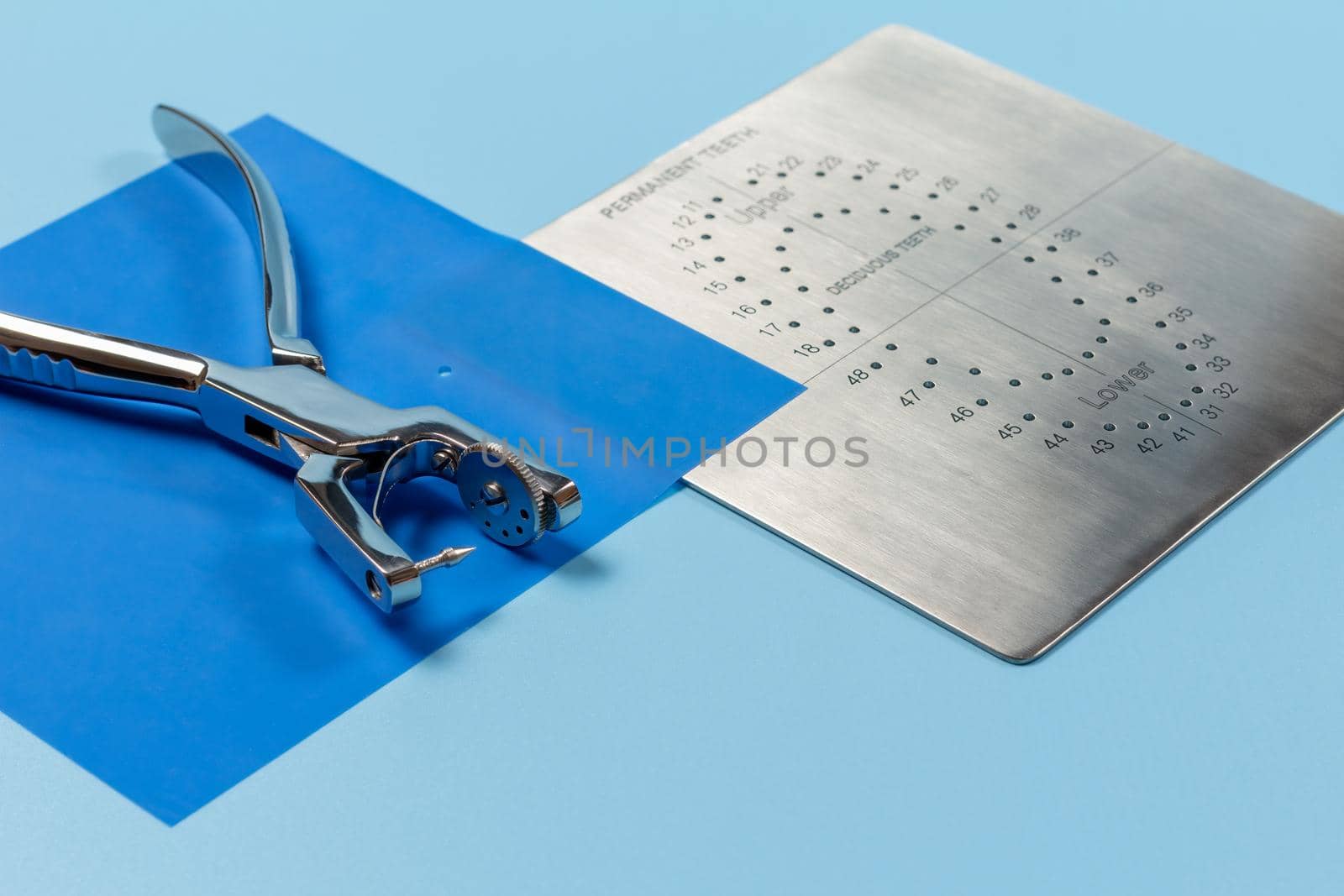 Dental hole punch, the rubber dam and the metal plate on the blue background. Medical tools concept.