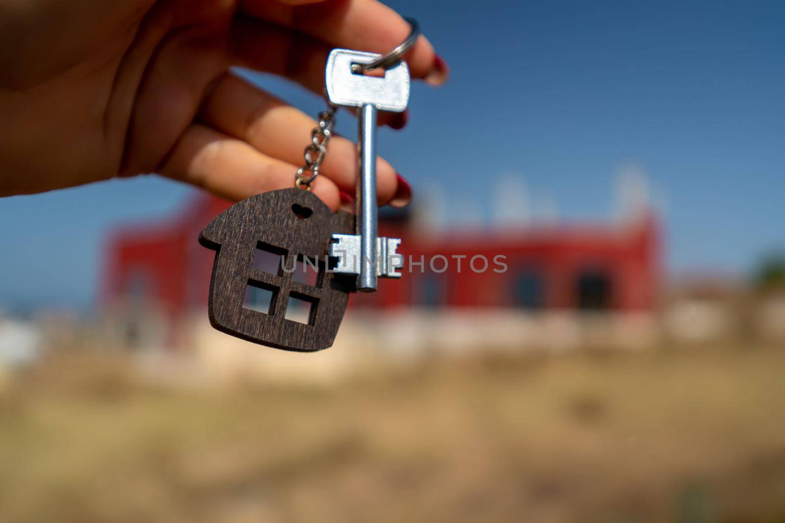 A woman's hand holds a house key against the backdrop of a house under construction. Real estate agent. Buying a house, apartment. by Matiunina