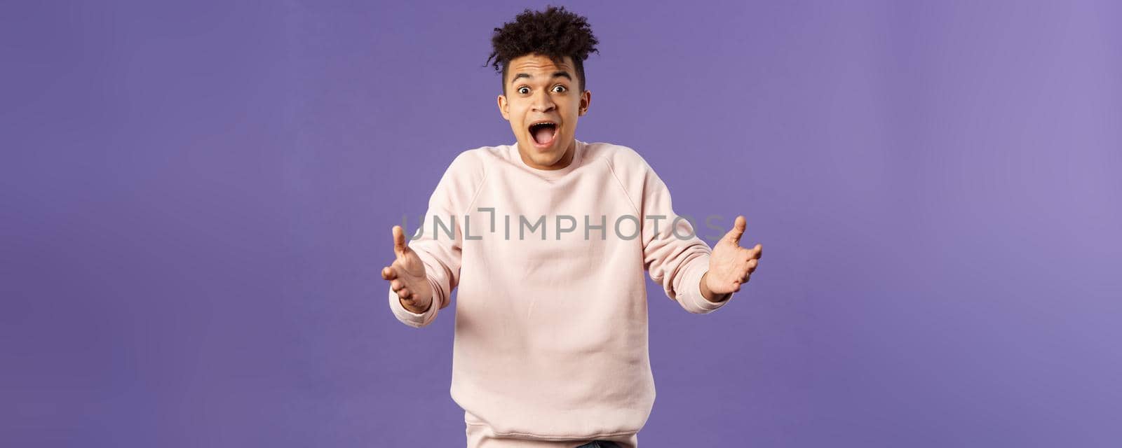 Portrait of surprised happy young man reaching hands to hug friend seeing him on street, rejoicing over big great news, standing impressed and thrilled over purple background.
