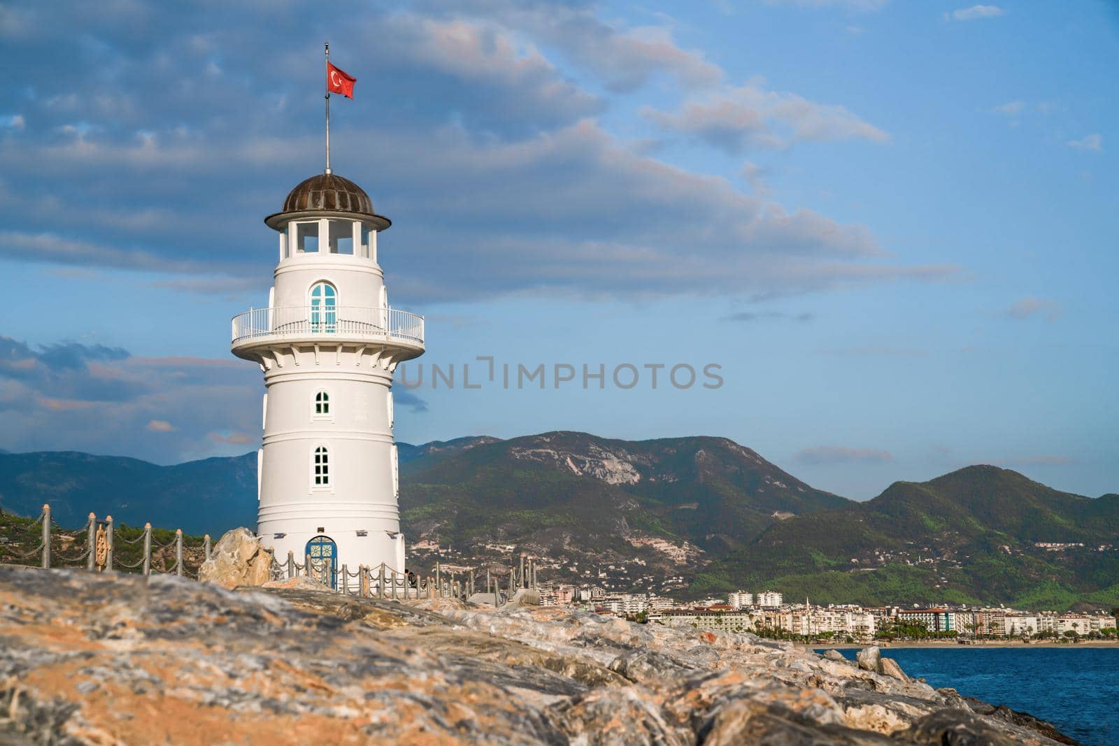 Turkey, Alanya - November 9, 2020: White port lighthouse on the background of mountains and sky and sea. Copy space