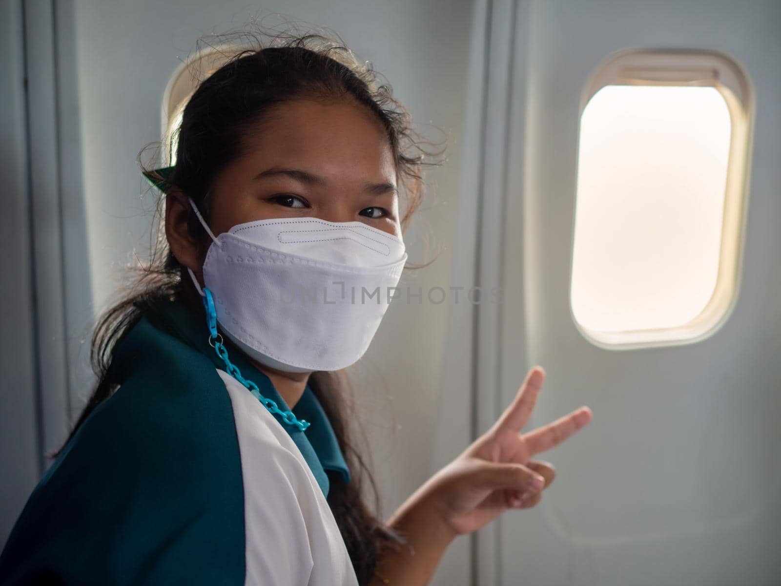 A woman wearing a mask is sitting by the window of an airplane.