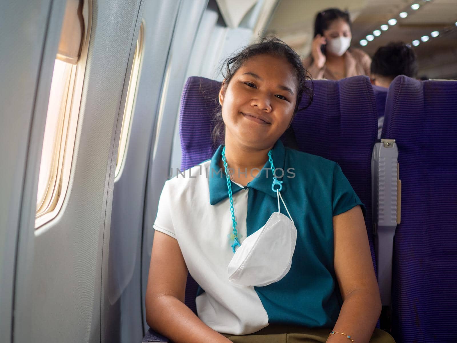 A woman wearing a mask is sitting by the window of an airplane.