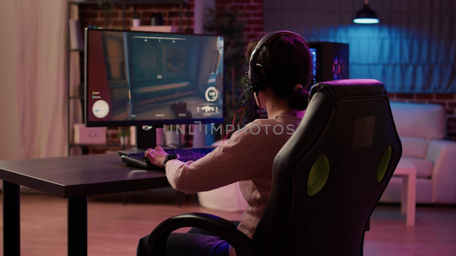 Gamer girl using pc gaming setup relaxing playing multiplayer online action game talking using headset by DCStudio