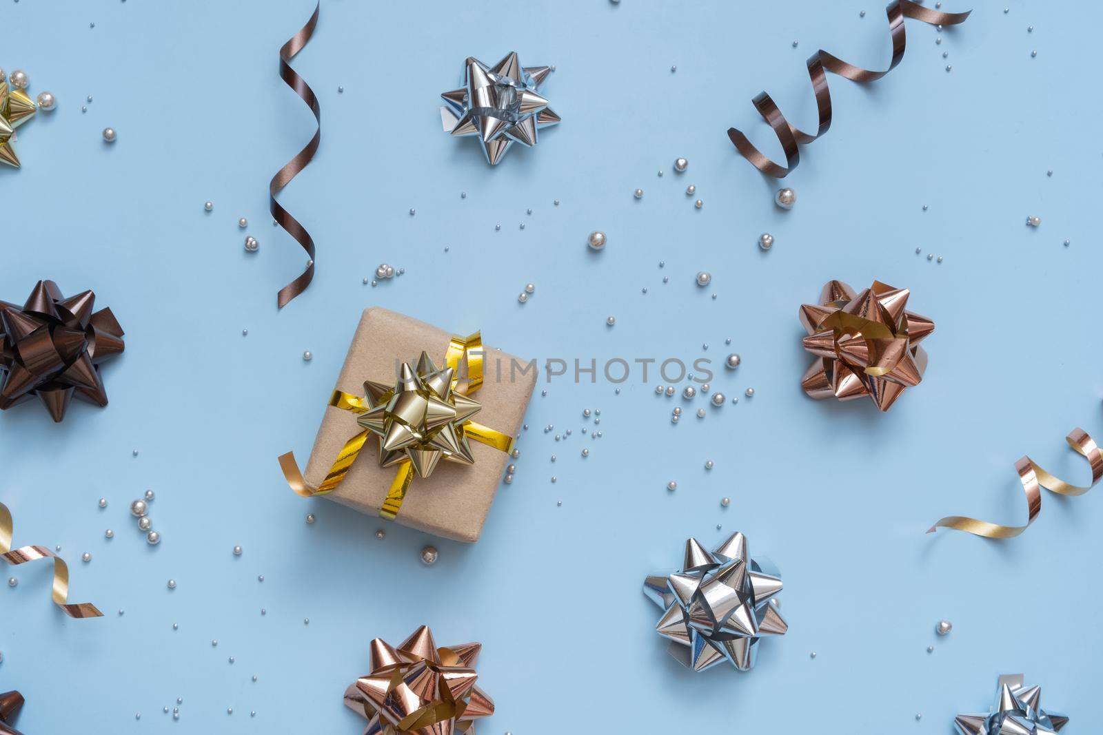 Gift box on bright festive background with bows and beads top view. Christmas gift flat lay.