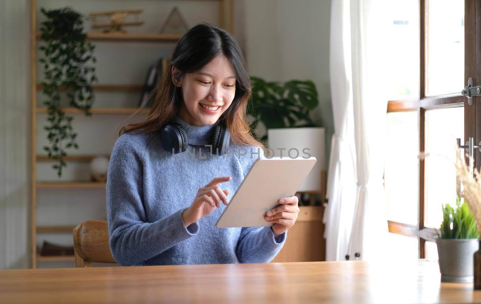 Portrait of smiling happy beautiful asian woman relaxing using technology of tablet while sitting on table.Young creative girl working and typing on keyboard at home.work at home concept.