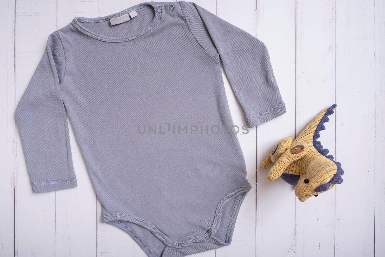 Grey baby bodysuit top view. Mock up for logo, text or design on wooden background. Flat lay with dinosaur by ssvimaliss