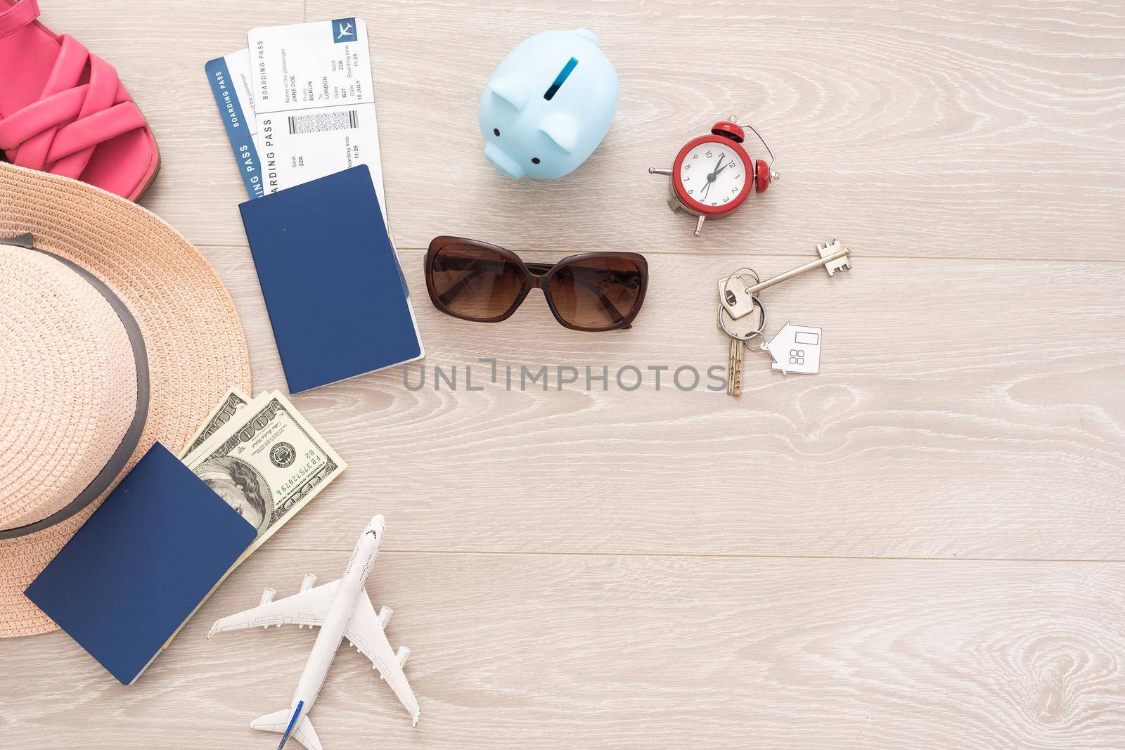 A piggy bank with dollar bills in a travel setting. In the composition of the image: Sun Hat, Alarm Clock. Concept of saving money for traveling on vacation. by Andelov13