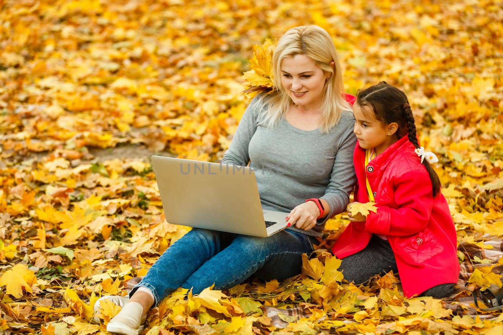 Happy mother and her tdaughter using laptop in the park. by Andelov13