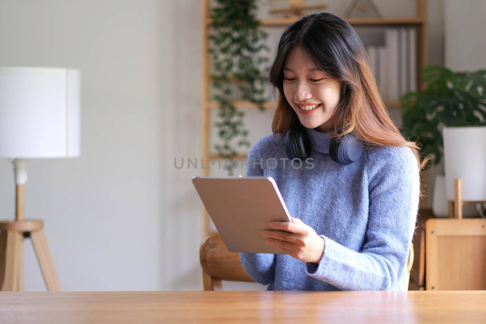 Portrait of smiling happy beautiful asian woman relaxing using technology of tablet while sitting on table.Young creative girl working and typing on keyboard at home.work at home concept by wichayada