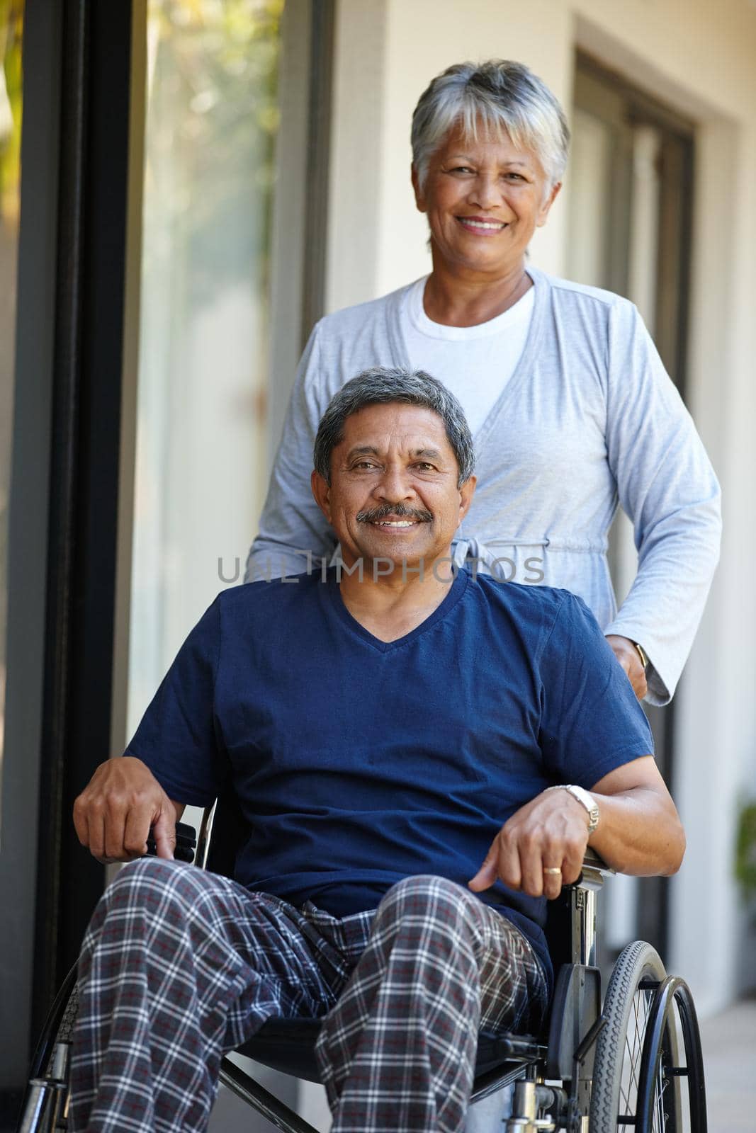 Shes my rock. Portrait of a senior woman pushing her husband in a wheelchair outdoors. by YuriArcurs