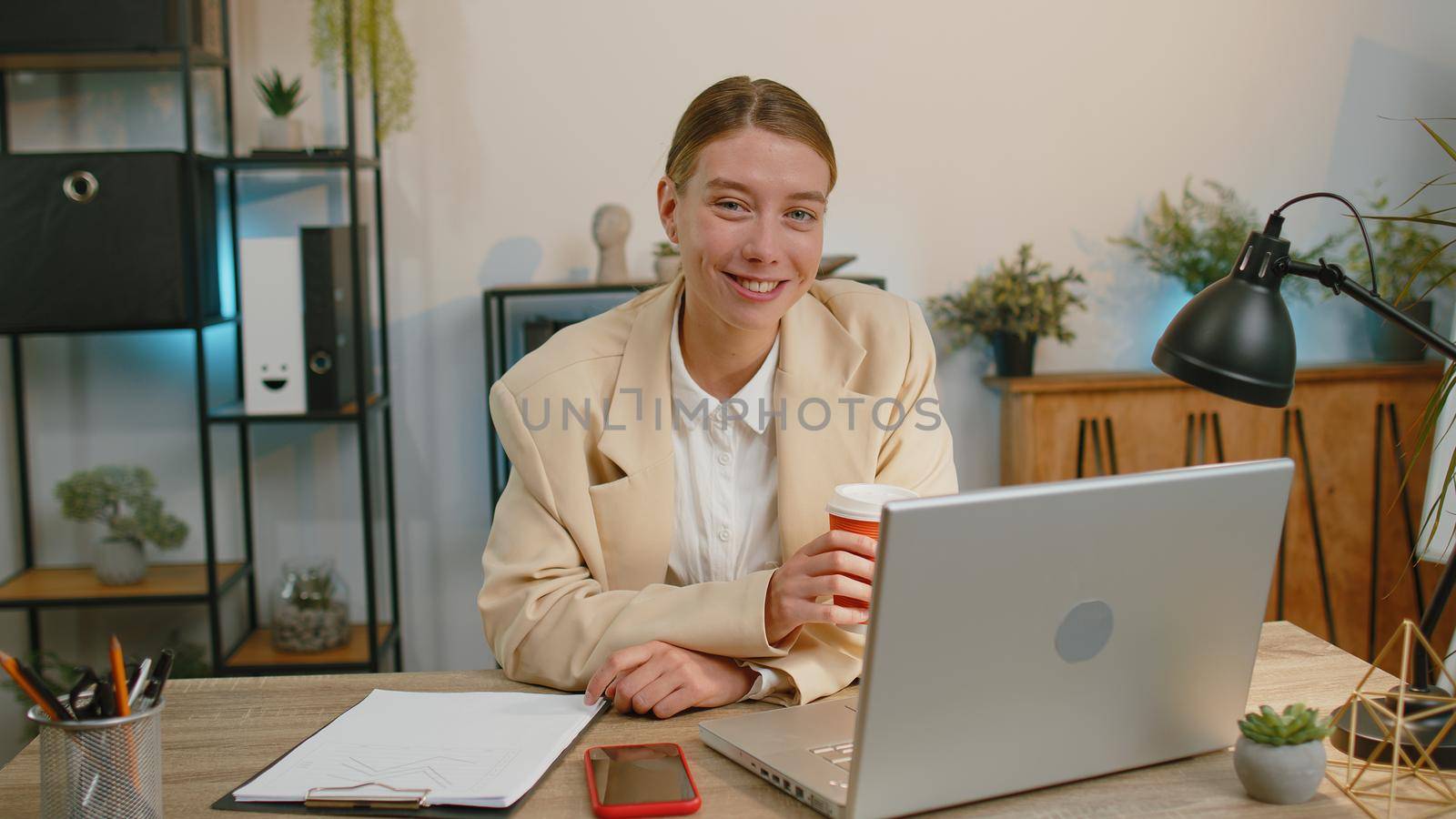 Businesswoman freelancer enters office start working on laptop computer at desk and drinking morning coffee. Woman works on notebook, sends messages makes online purchases watching social media movies