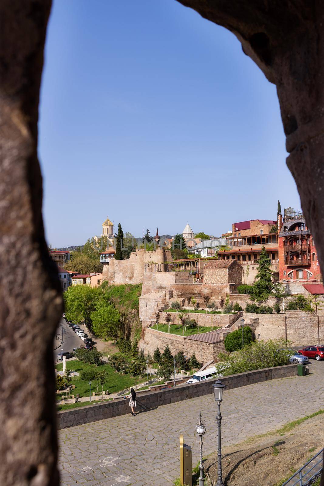 View of the old city of tbilisi through a round window in a thick stone wall