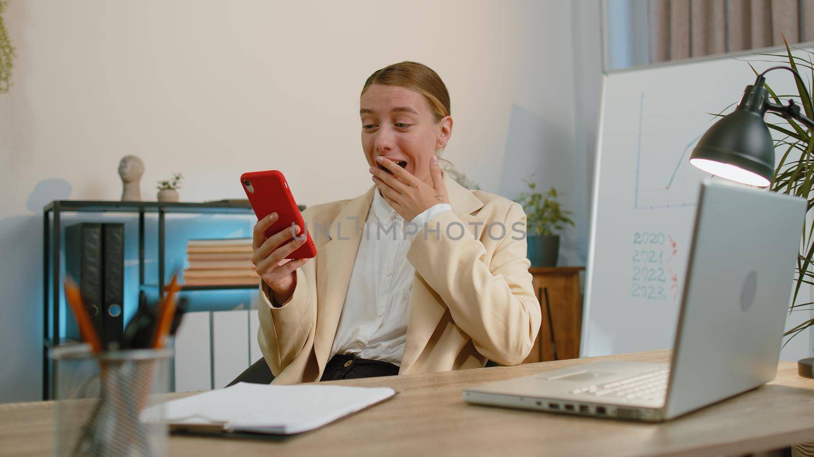 Business woman programmer software developer working at office finishing up phone call selling online using smartphone, making victory gesture receiving good news rejoicing over success triumph