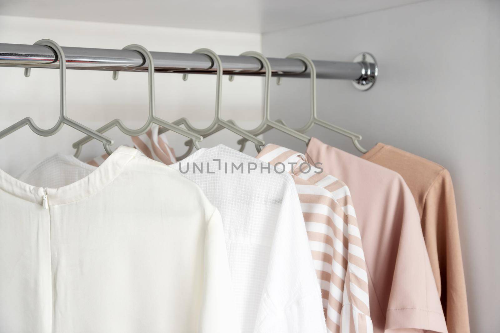 Colored clothes hang on a hanger in a home closet or store. Shirts, blouses, jackets, different colors. The concept of a clothing store, the work of a stylist in the selection of clothes