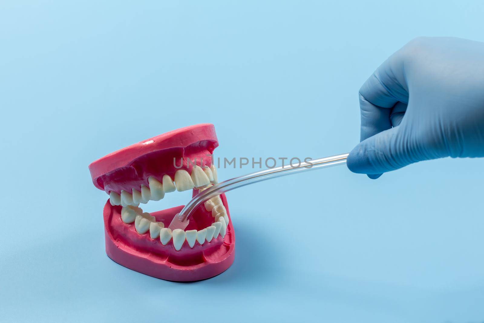 Dentist's hand in a latex glove with the saliva ejector and the human jaw layout on the blue background. Medical tools concept.