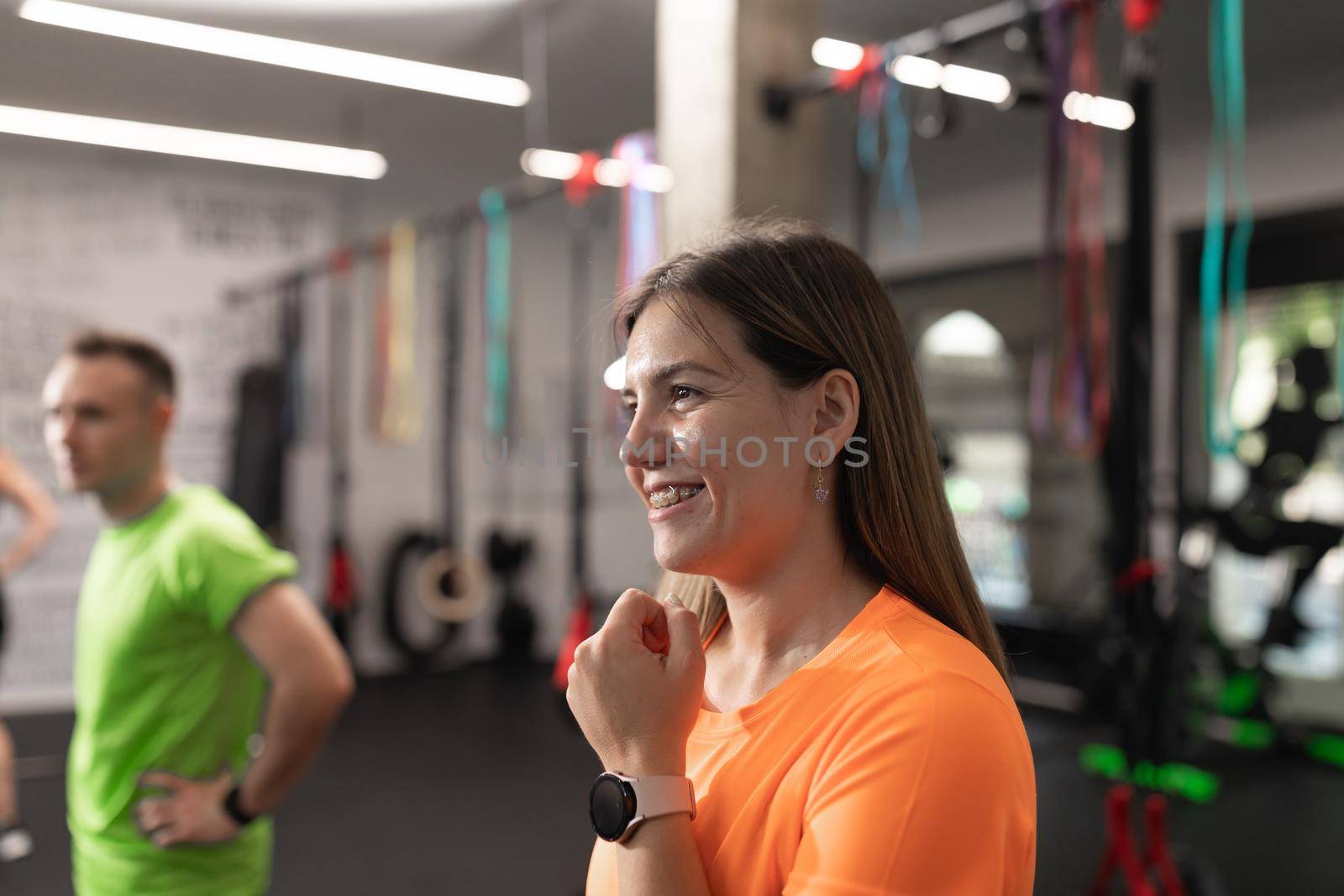 Portrait of a female trainee smiling and placing her wrostwatch while resting during a workout at the gym