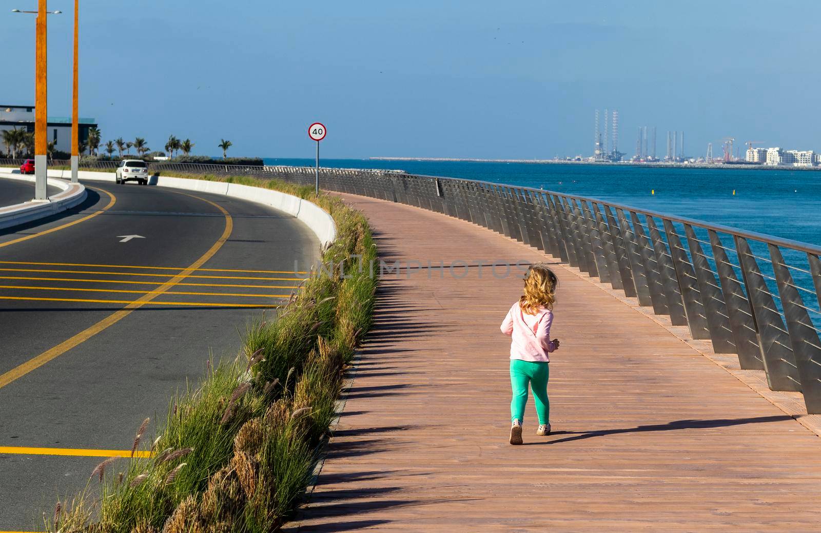 little girl running on a boardwalk next to the road