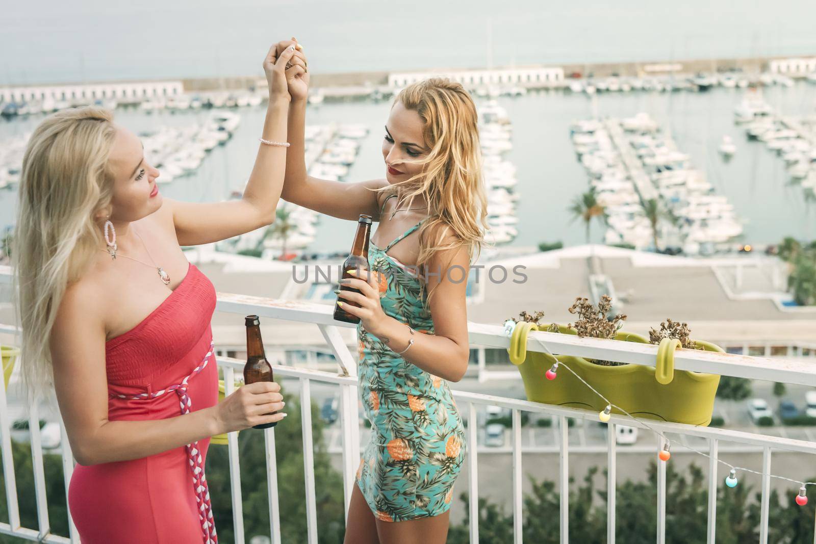 carefree young girls with beers dancing and having fun at a private party on the outdoor terrace in front of the port, leisure happiness and friendship concept