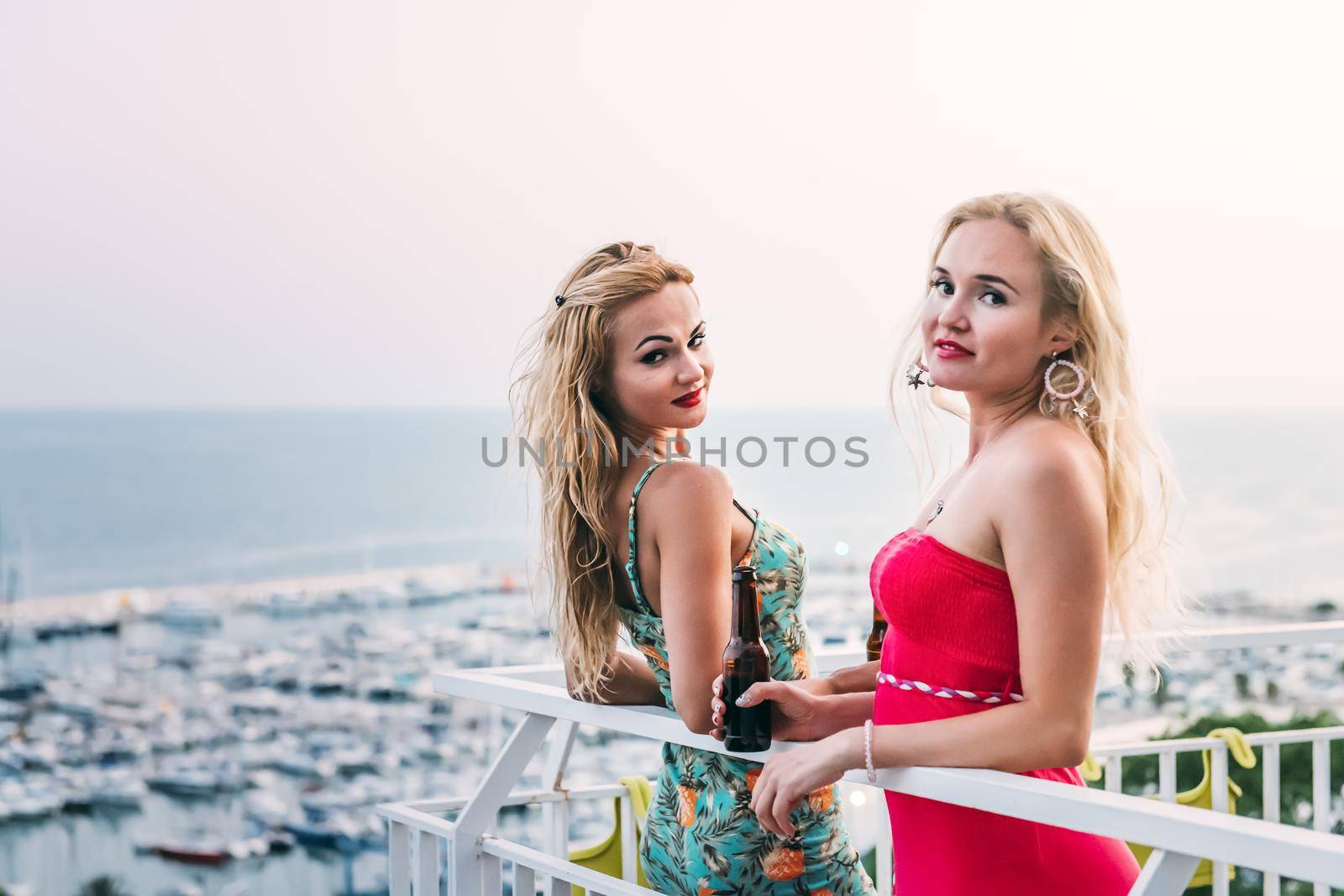 pretty young girls with beers posing and having fun at a private party on the outdoor terrace in front of the port, leisure happiness and friendship concept, copy space for text