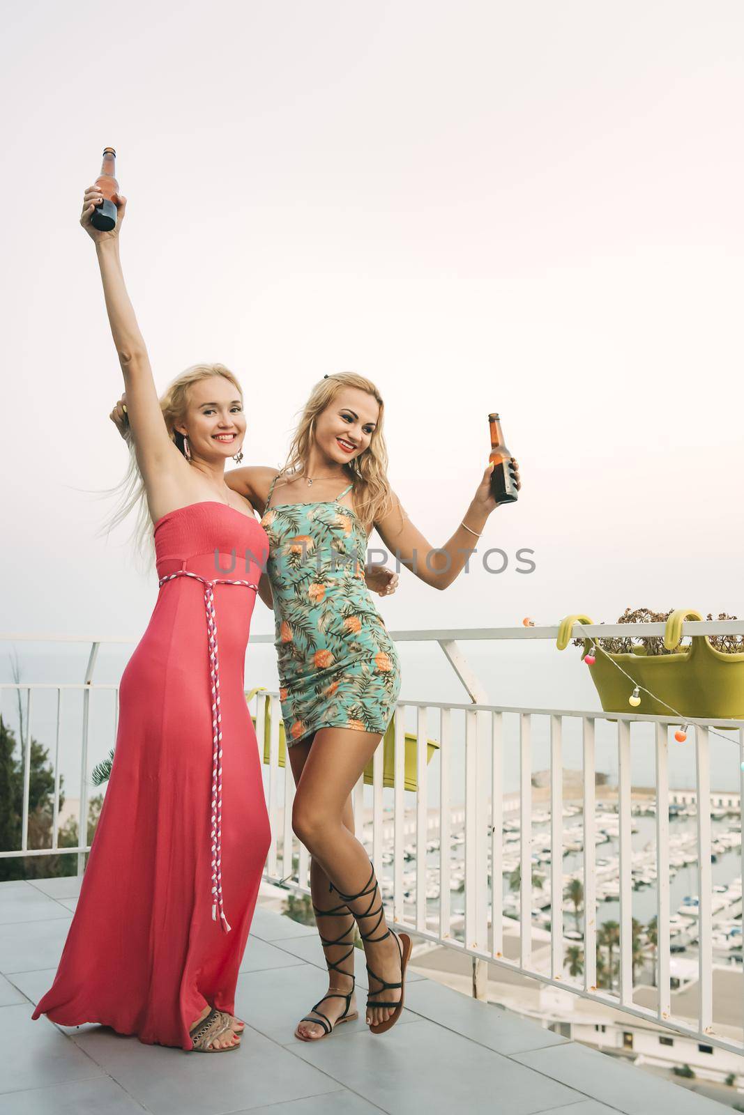carefree young girls with beers dancing and having fun at a private party on the outdoor terrace in front of the port, leisure happiness and friendship concept, vertical photo with copy space for text