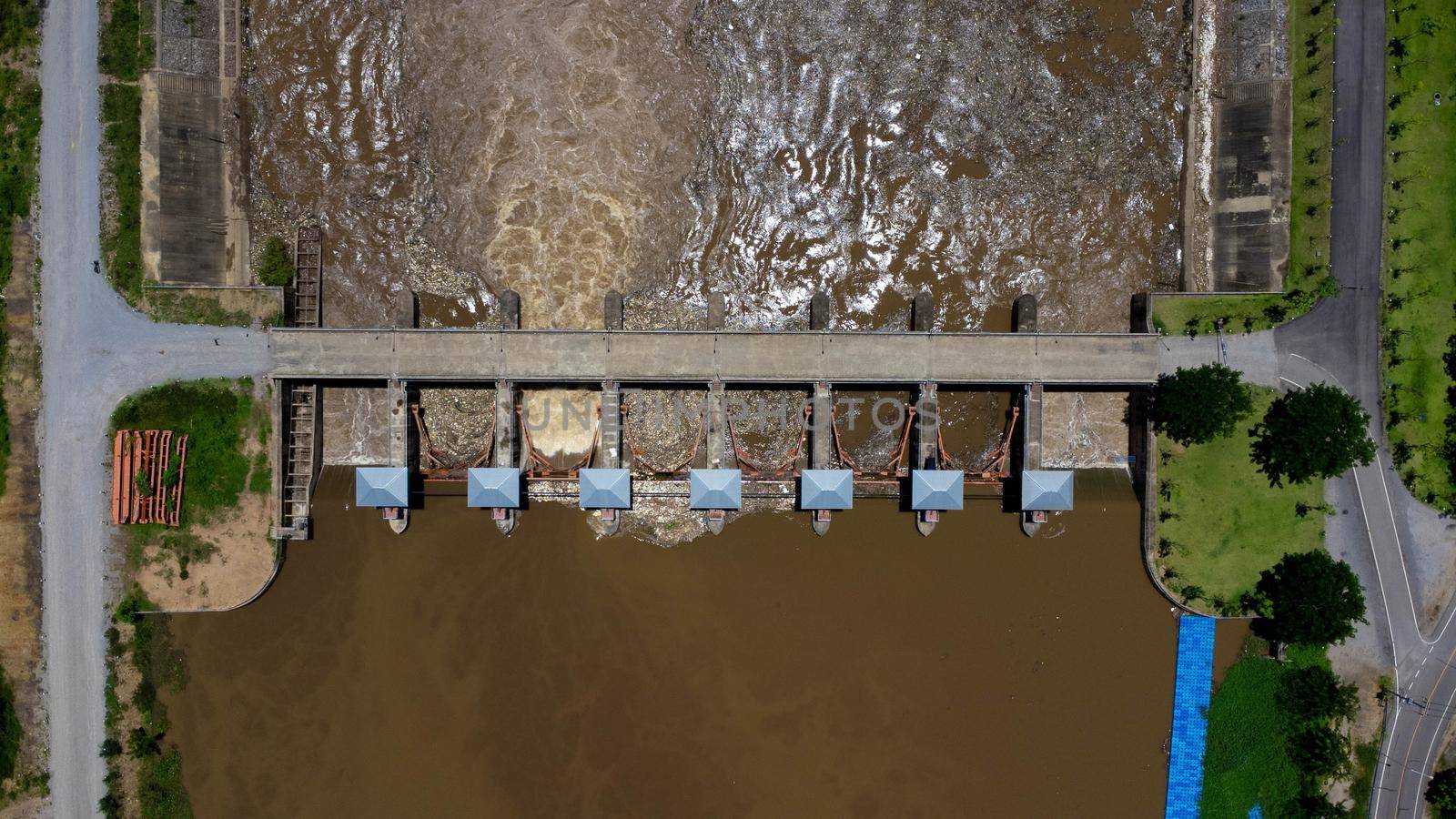 Aerial view of the water released from the concrete dam's drainage channel as the overflow in the rainy season. Top view of turbid brown forest water flows from a dam in rural northern Thailand. by TEERASAK