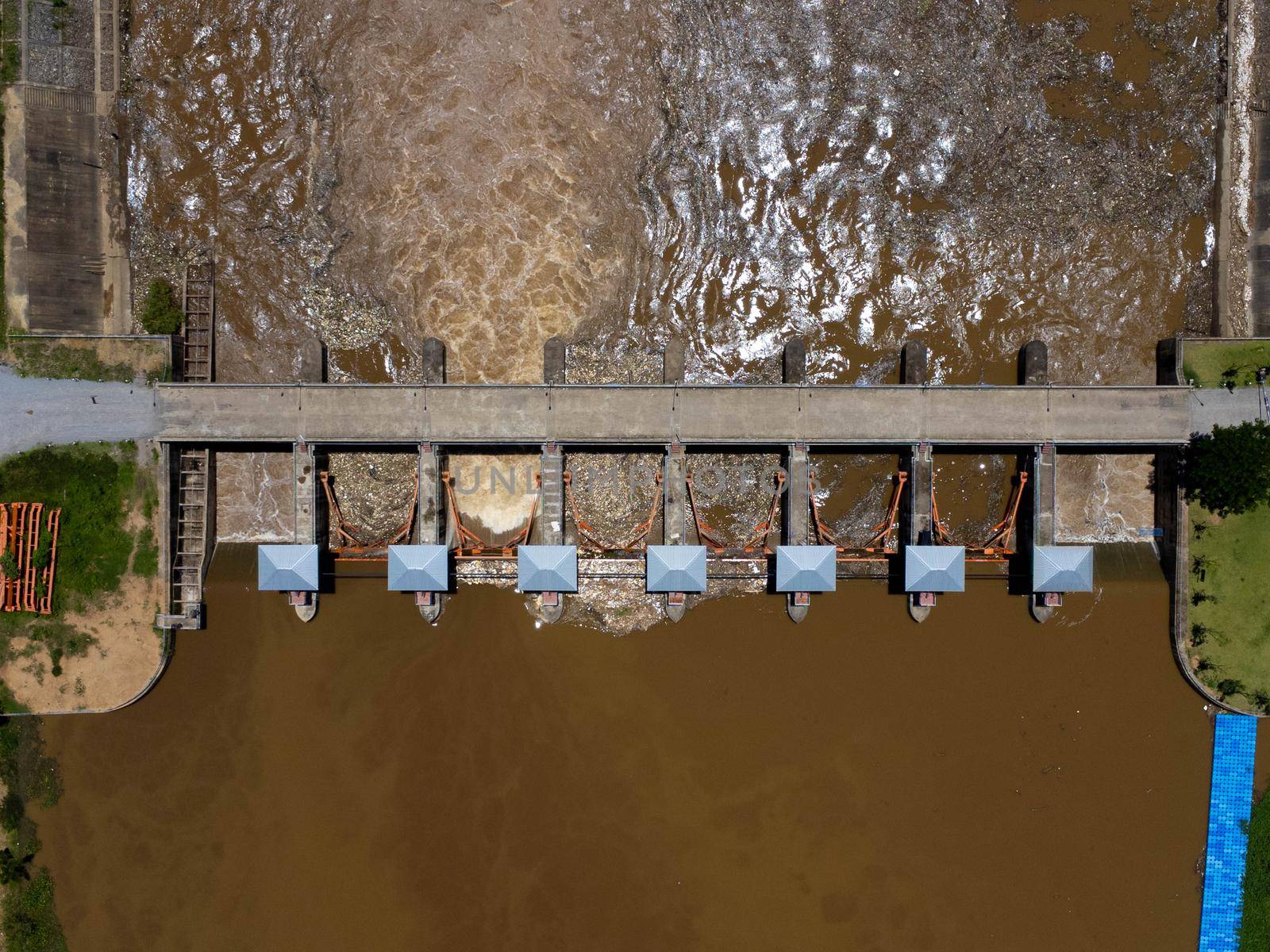 Aerial view of the water released from the concrete dam's drainage channel as the overflow in the rainy season. Top view of turbid brown forest water flows from a dam in rural northern Thailand.