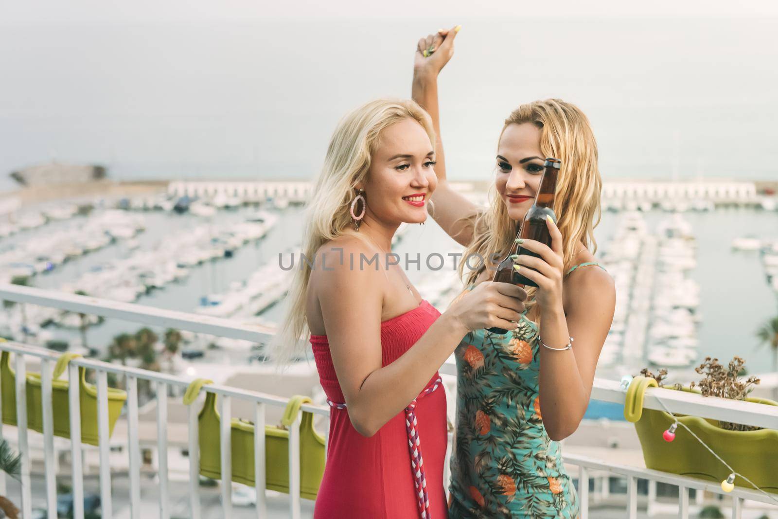carefree young girls with beers dancing and having fun at a private party on the outdoor terrace, leisure happiness and friendship concept