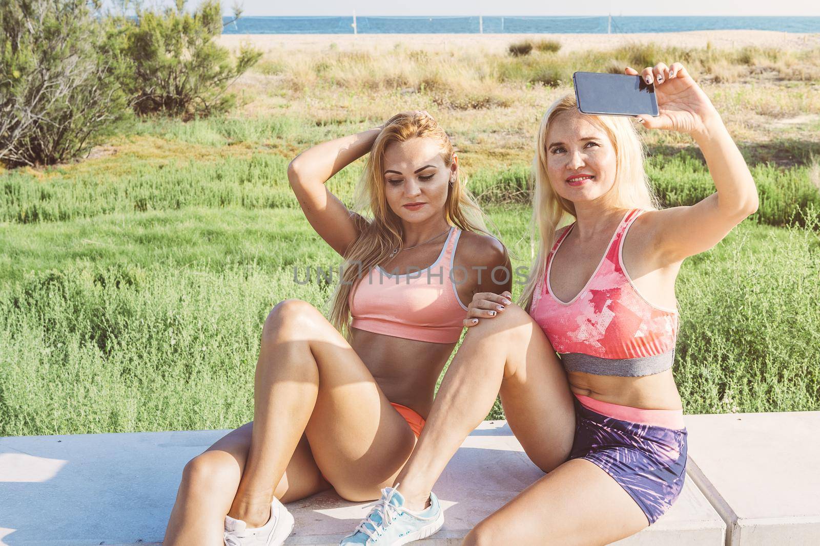 two attractive female athletes smiling as they take a selfie with the phone, sports women taking a break during training, fitness and healthy lifestyle concept