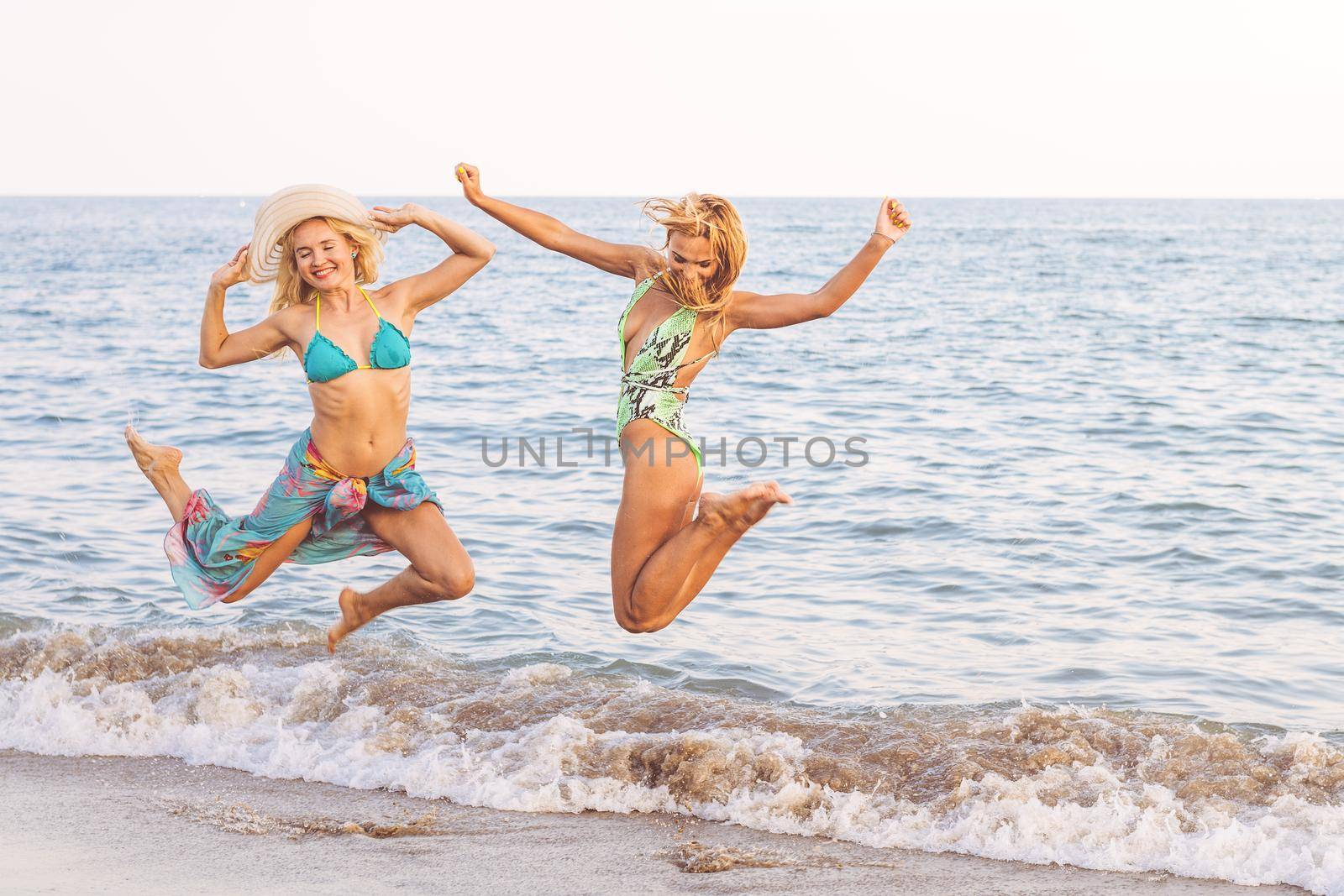 couple of two blonde girls jumping on the shore of the beach, concept of friendship and relaxation in the summer