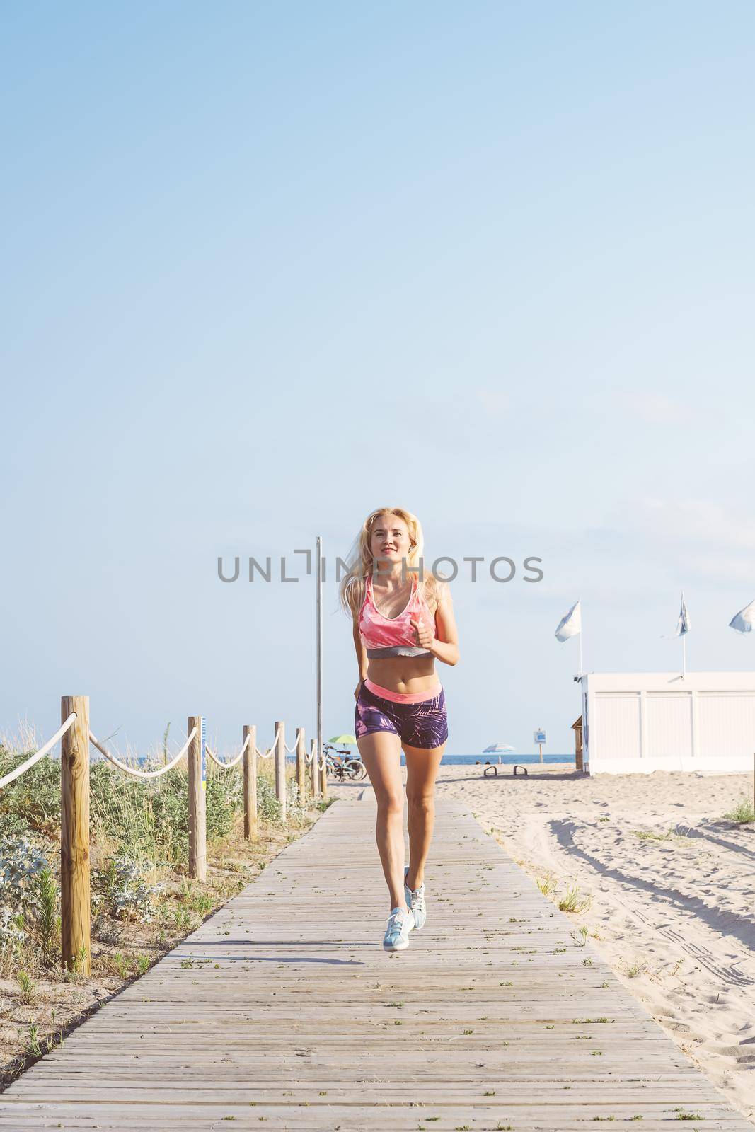 attractive female athlete training for the promenade, blonde sporty woman running, fitness and healthy lifestyle concept, dynamic movement, vertical photo with copy space for text