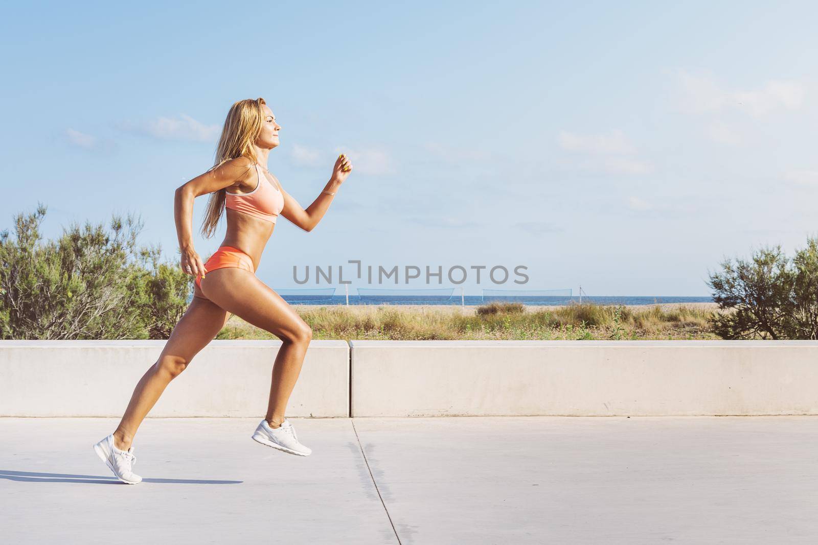 beautiful blonde female athlete running fast for the promenade, athletic sportswoman training, fitness and healthy lifestyle concept, dynamic movement, vertical photo with copy space for text